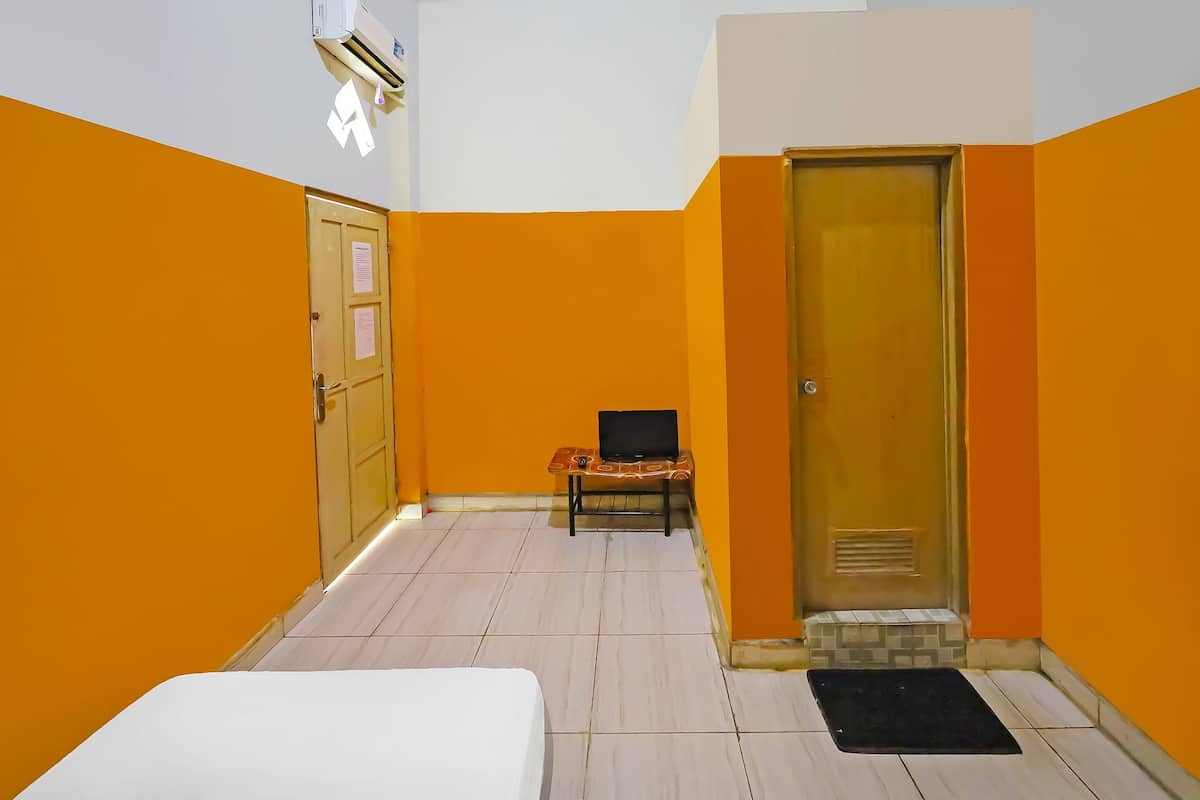 A hotel room with orange walls, a bed, a desk with a chair, and a door.