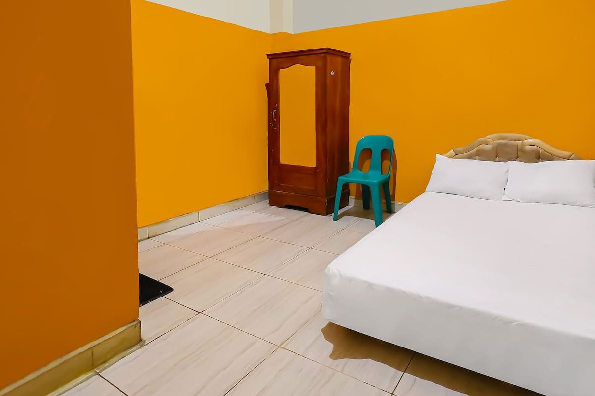 A room with a bed, a wooden wardrobe, and a plastic chair.