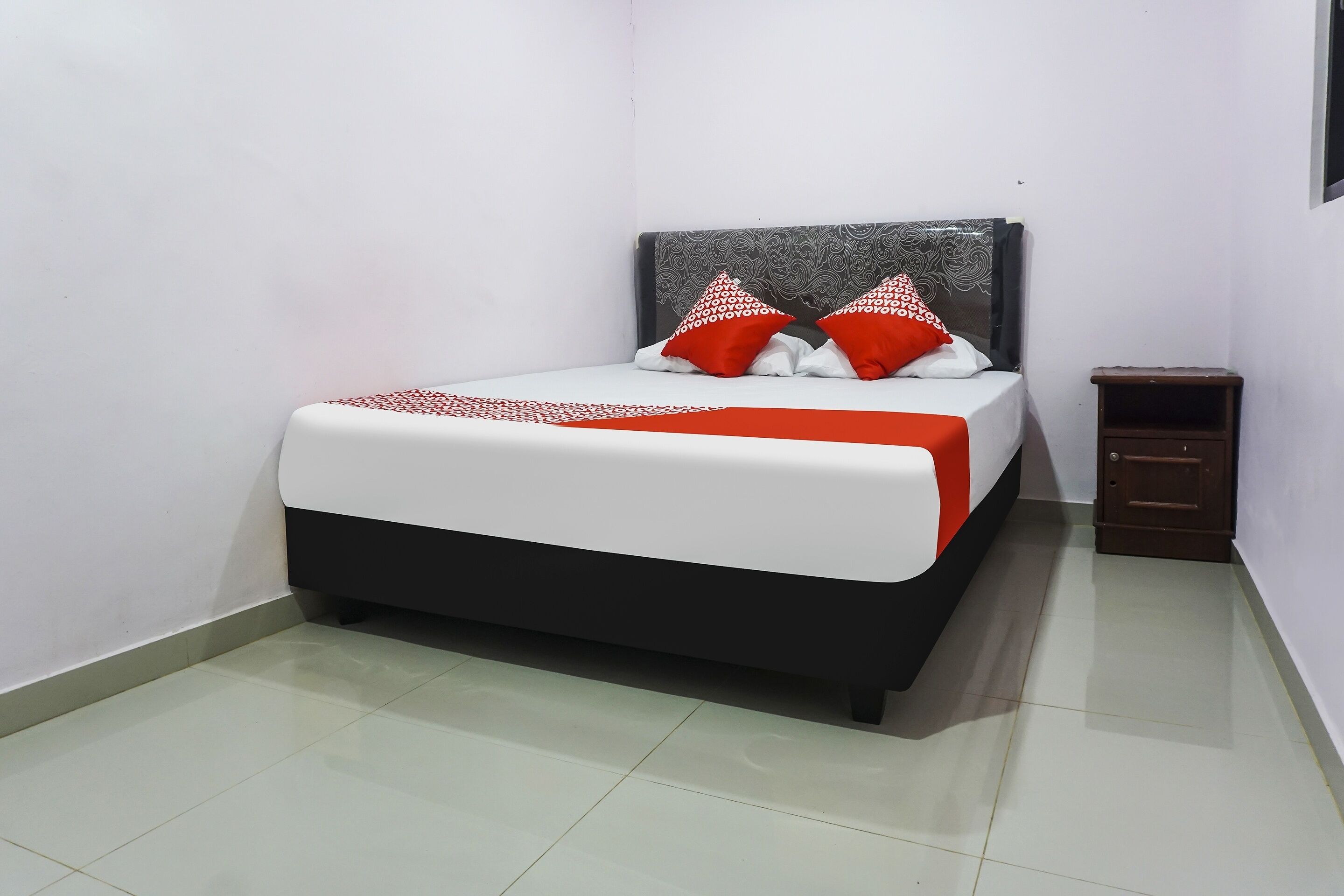 A neatly made bed with a white and red bedspread, two red and white pillows, and a dark headboard.