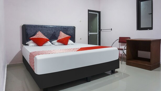 A neatly arranged bedroom with a bed, a door, a chair, and a small wooden table. - Hotel O Homestay Madu Makassar (Makassar)