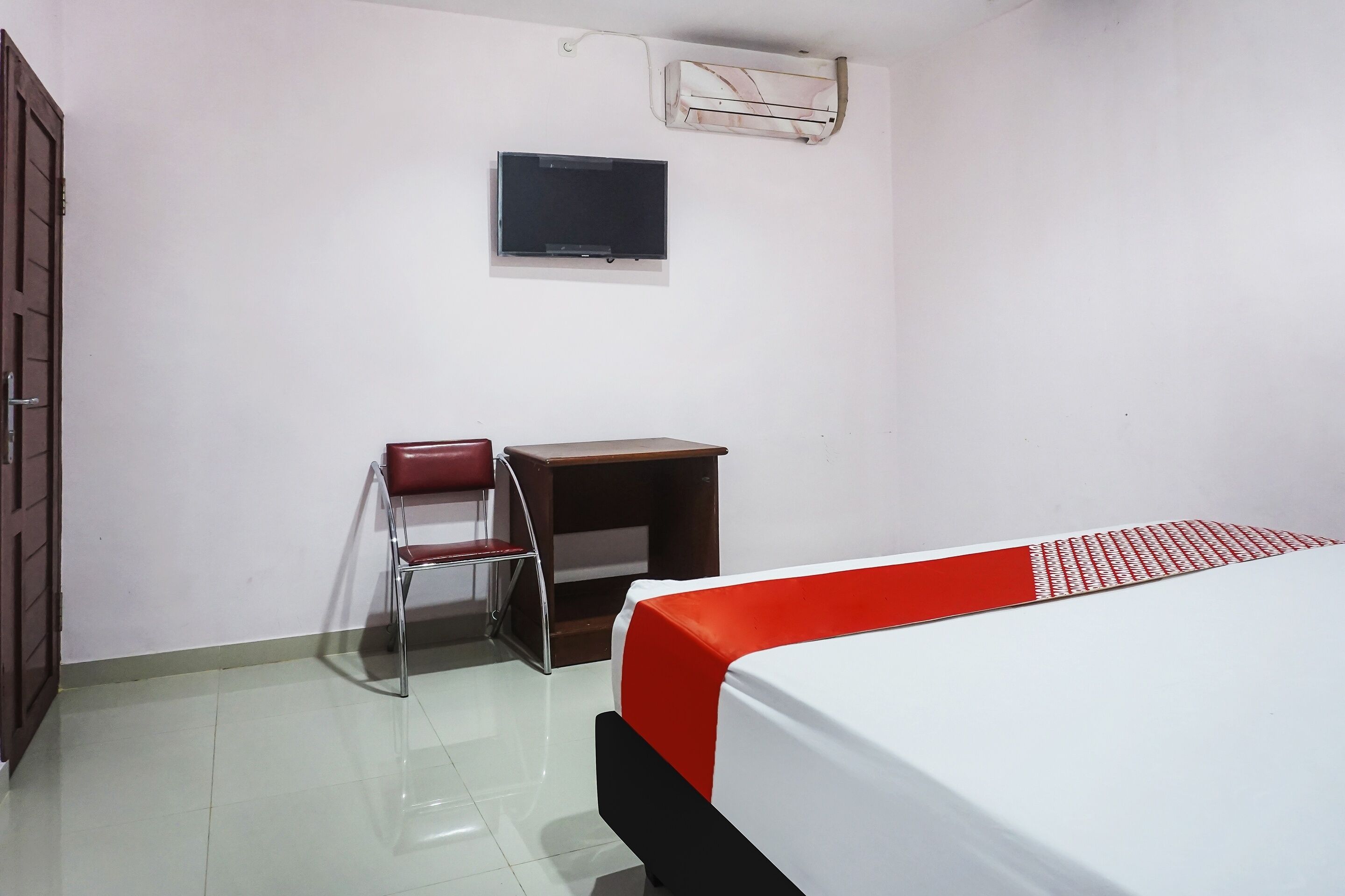 A room with a bed, a desk, a chair, and a television on the wall.
