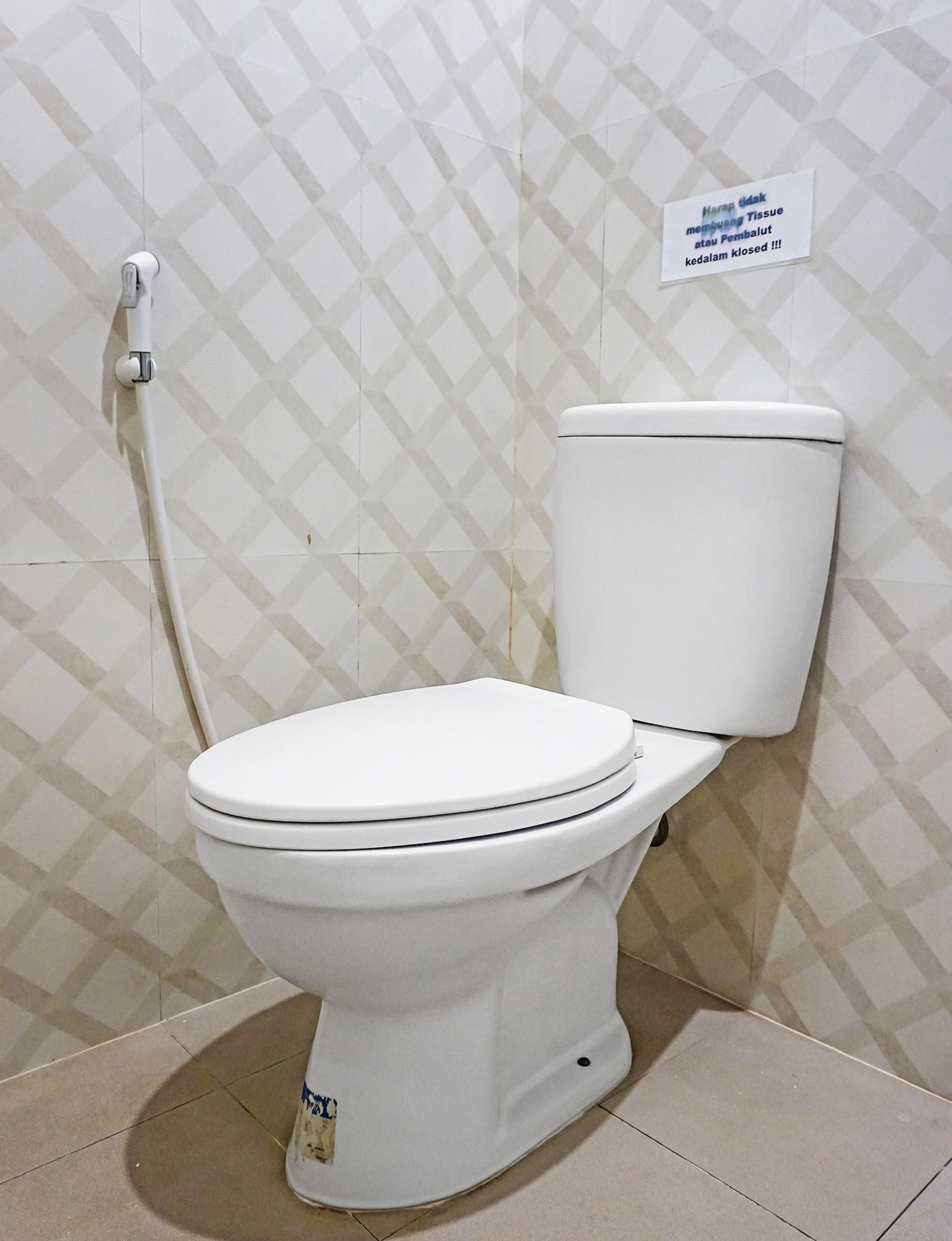 A white toilet with a closed lid, a white pipe, and a sign on the wall.