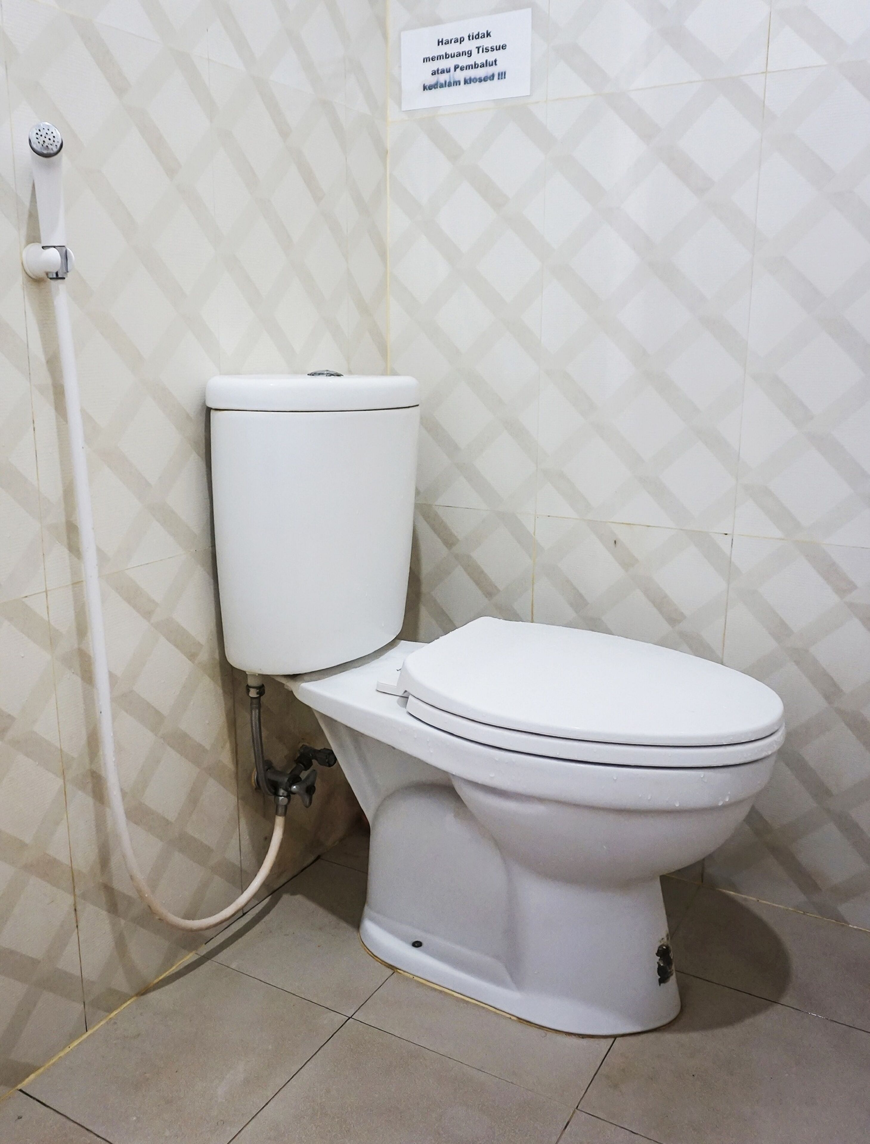 A toilet with a white tank and seat, a visible pipe, and a wall with a geometric pattern.