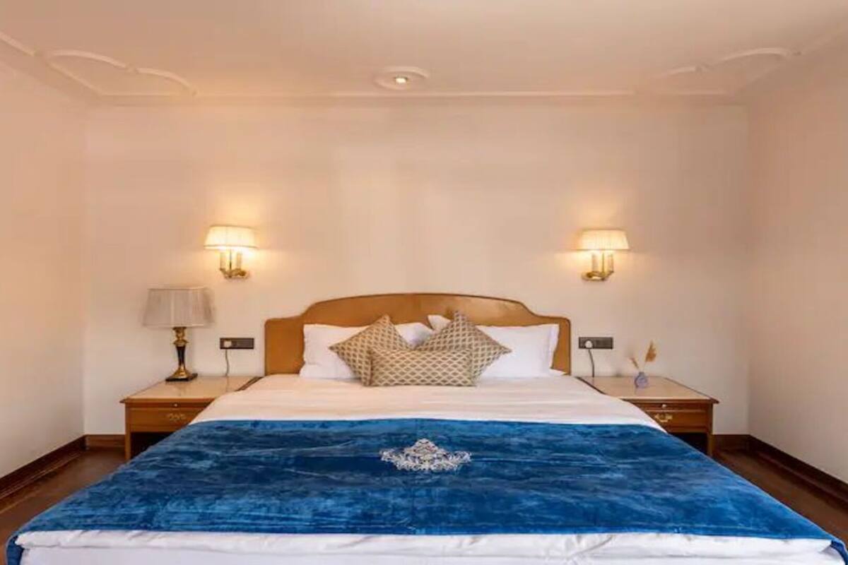 A hotel room with a large bed, two bedside lamps, and a nightstand with a lamp.