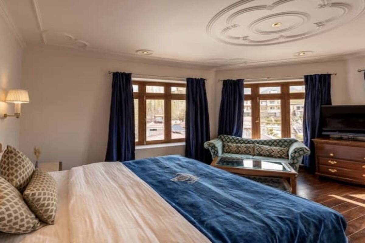 A hotel room with a bed, a sofa, a TV, and a window with curtains.