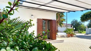 Ein modernes Haus mit überdachter Terrasse, Holzläden und Topfpflanzen.