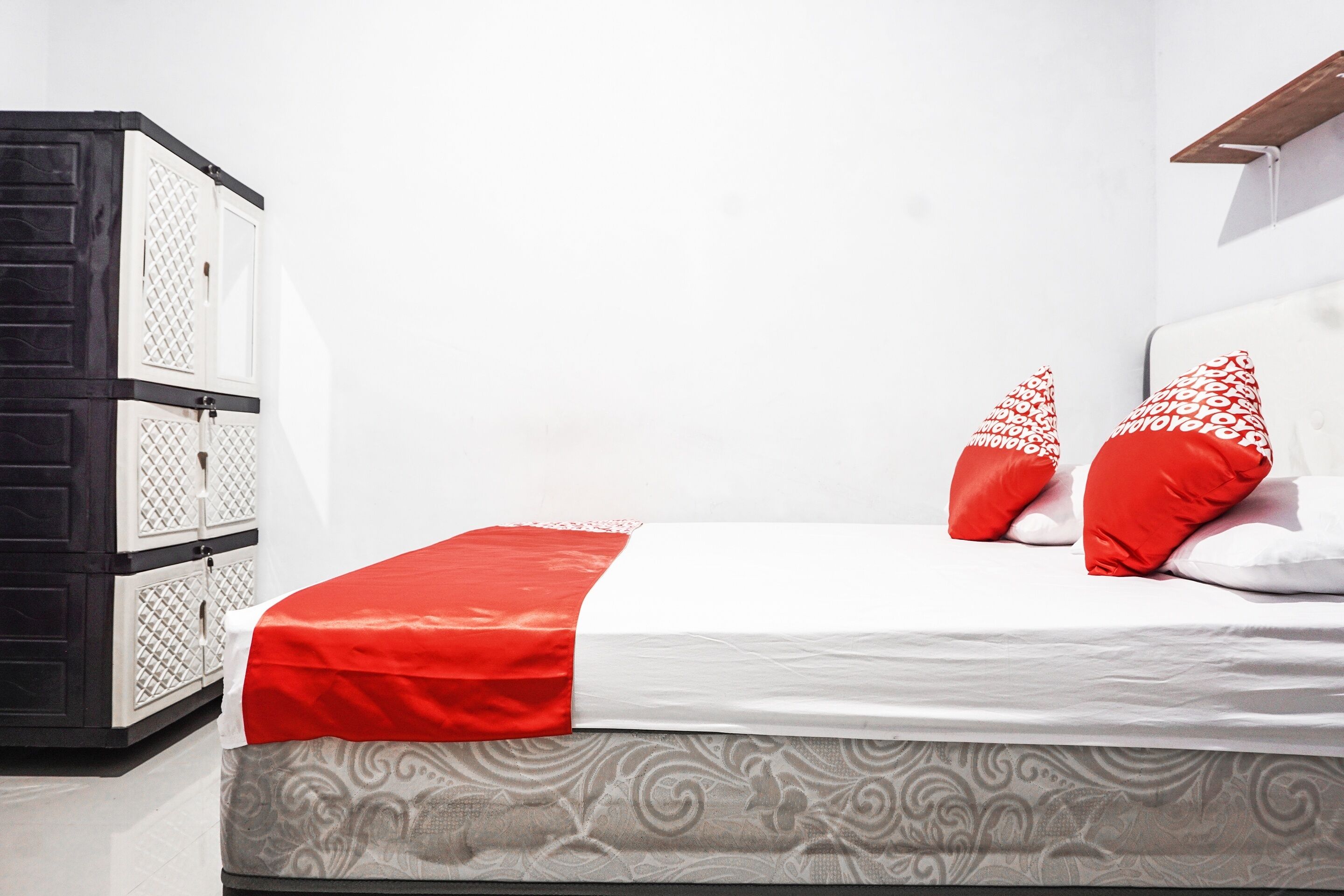 A bed with a white and red bedspread, two red pillows with white patterns, and a white headboard.