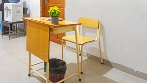 Un escritorio de madera con una silla, un cubo de basura y una planta en maceta sobre el escritorio.
