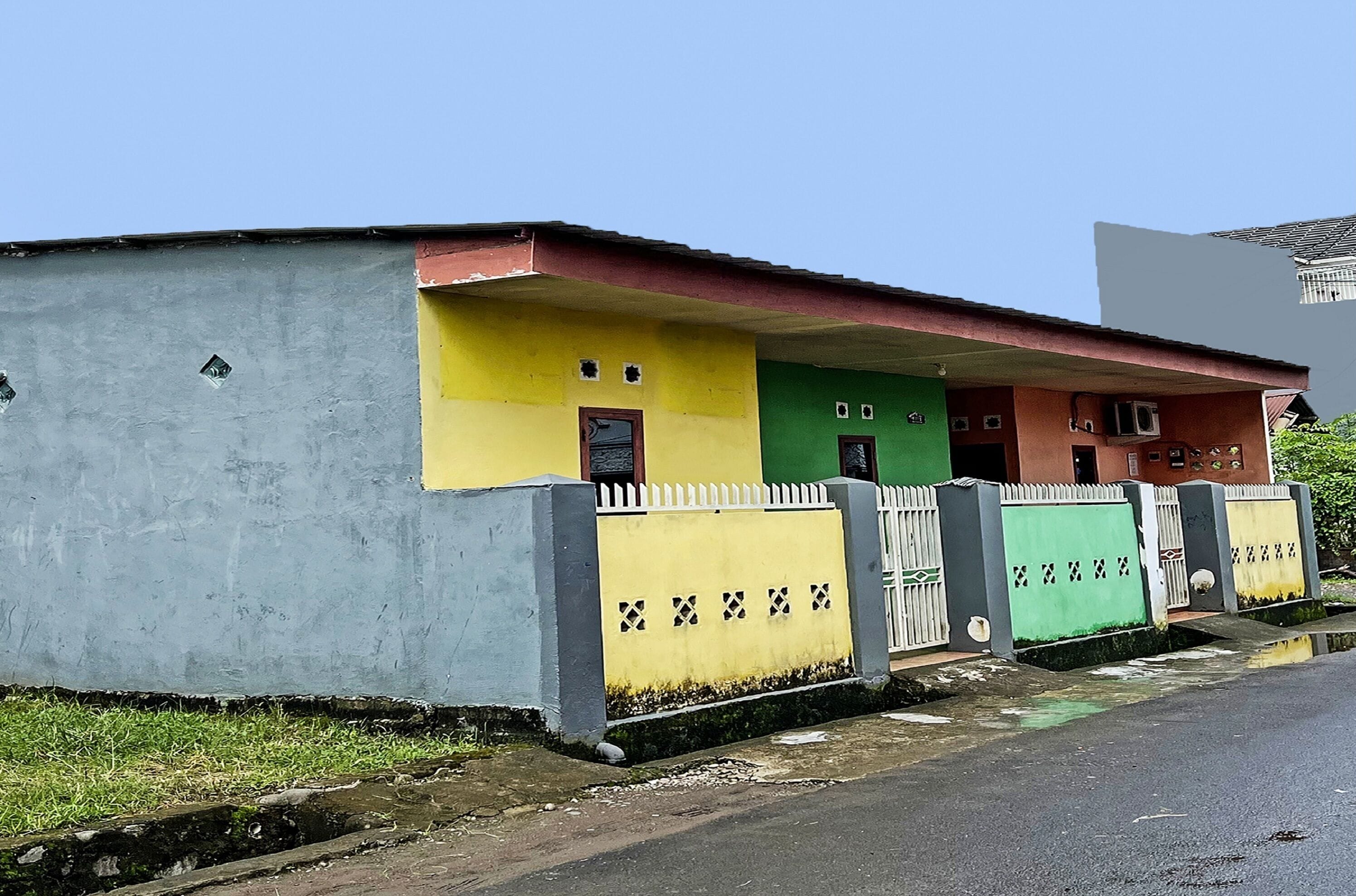 A building with a yellow, green, and red facade, a white picket fence, and a gated entrance.