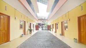 A corridor with a tiled floor, wooden doors, and a central open space with a view of the outside. - Hotel O A2b Guesthouse (Manado)