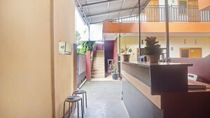 A narrow corridor with a reception desk, two stools, and a staircase leading to an upper floor. - Hotel O A2b Guesthouse (Manado)