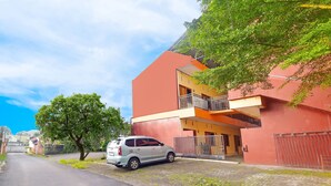A building with a red facade, a balcony, and a parked car. - Hotel O A2b Guesthouse (Manado)