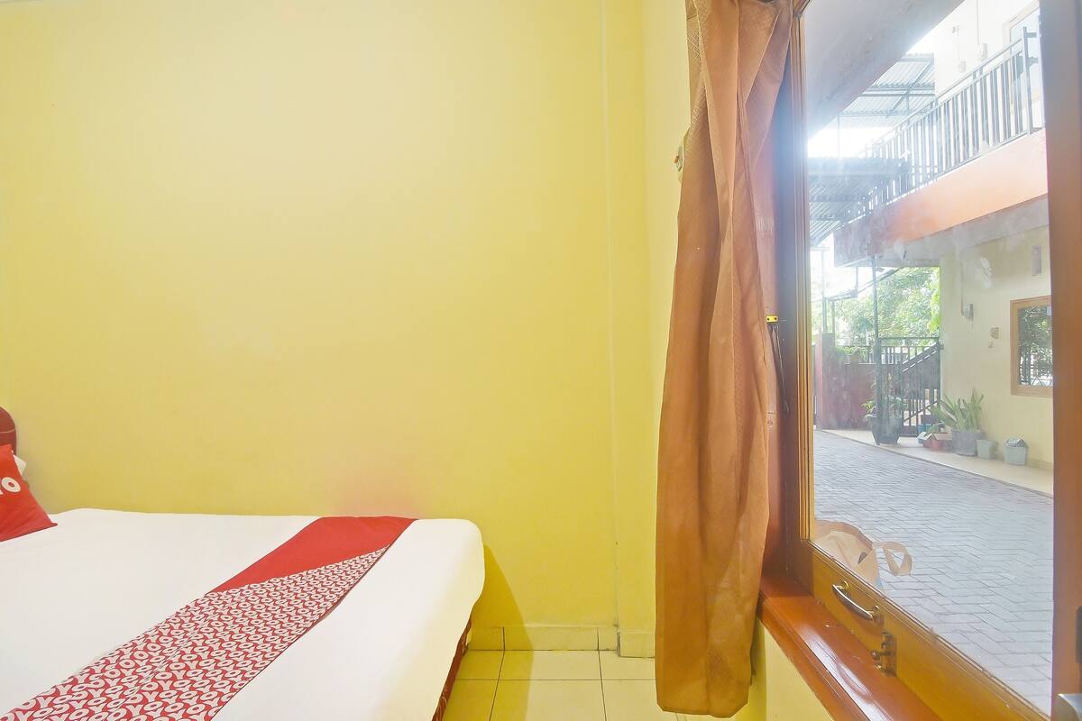 A hotel room with a bed, a window with curtains, and a view of the street outside.