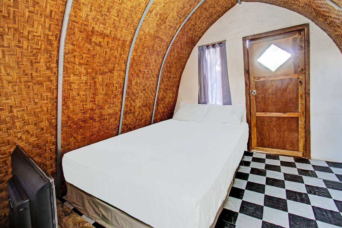 A room with a checkered floor, a bed with white bedding, a wooden door, and a television on the left.