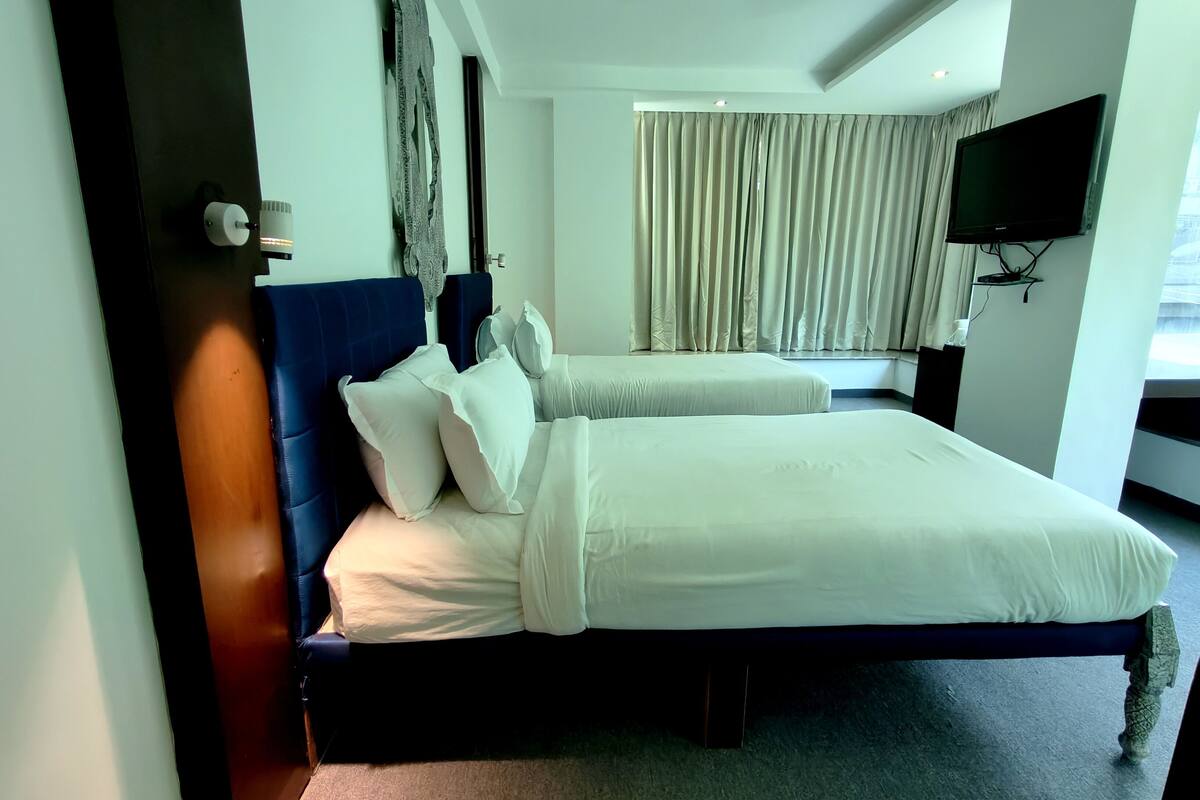 Een hotelkamer met twee bedden, een flatscreen televisie, een raam met gordijnen en een plafondventilator.