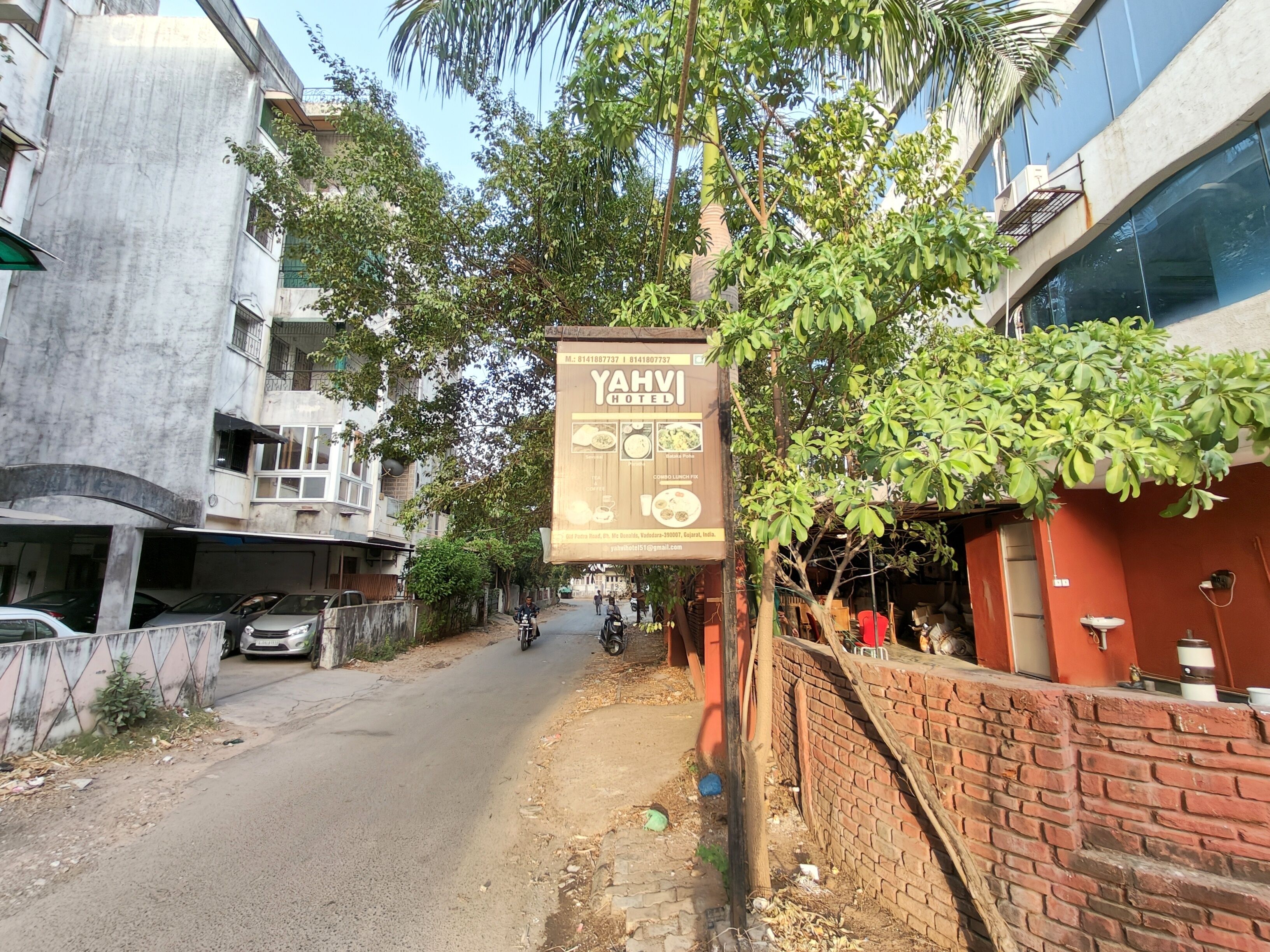 A street view with a sign for YAHVI HOTEL, featuring a contact number and email address.