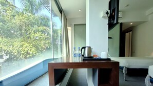 Hotelkamer met een groot raam, een houten tafel met waterkoker en flesjes water, een bed en een klein beeldje.