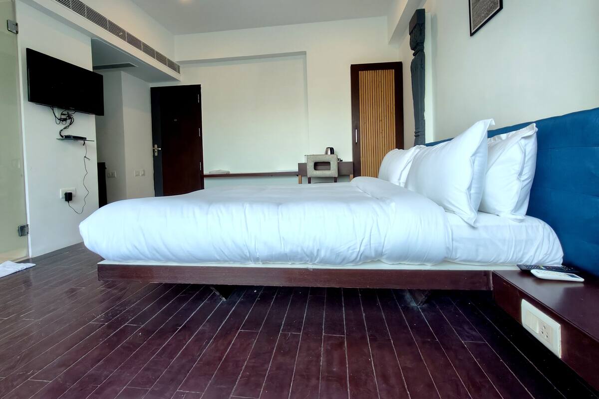 Een moderne hotelkamer met een groot bed, een flatscreen televisie aan de wand, een houten vloer en een klein nachtkastje.