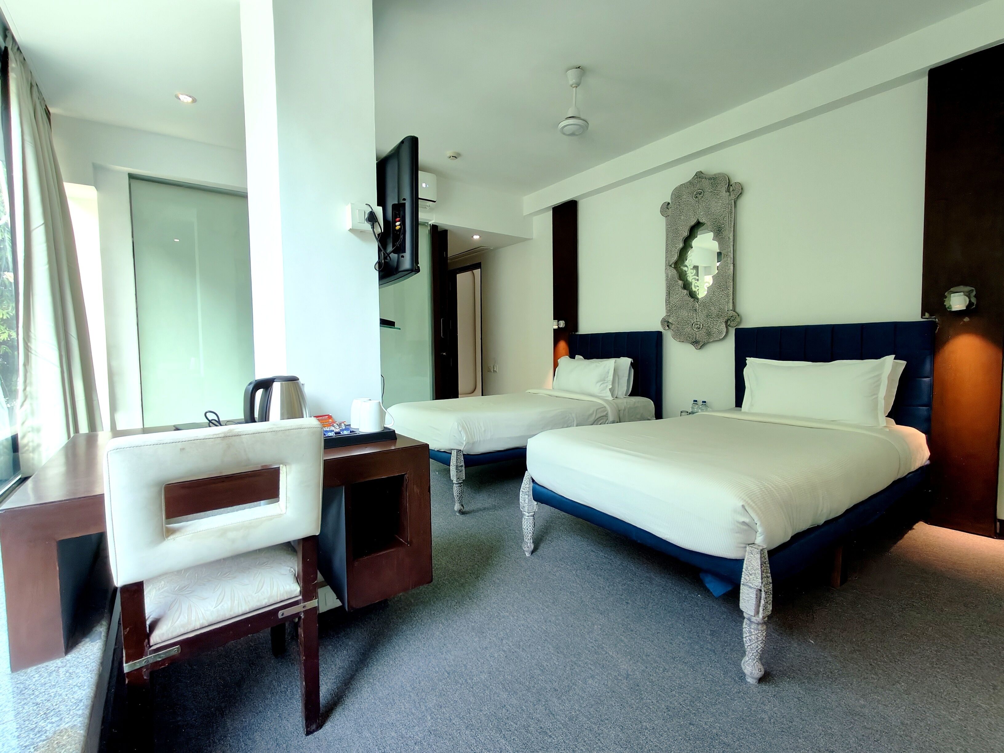 A hotel room with a desk, two beds, a mirror, and a ceiling fan.