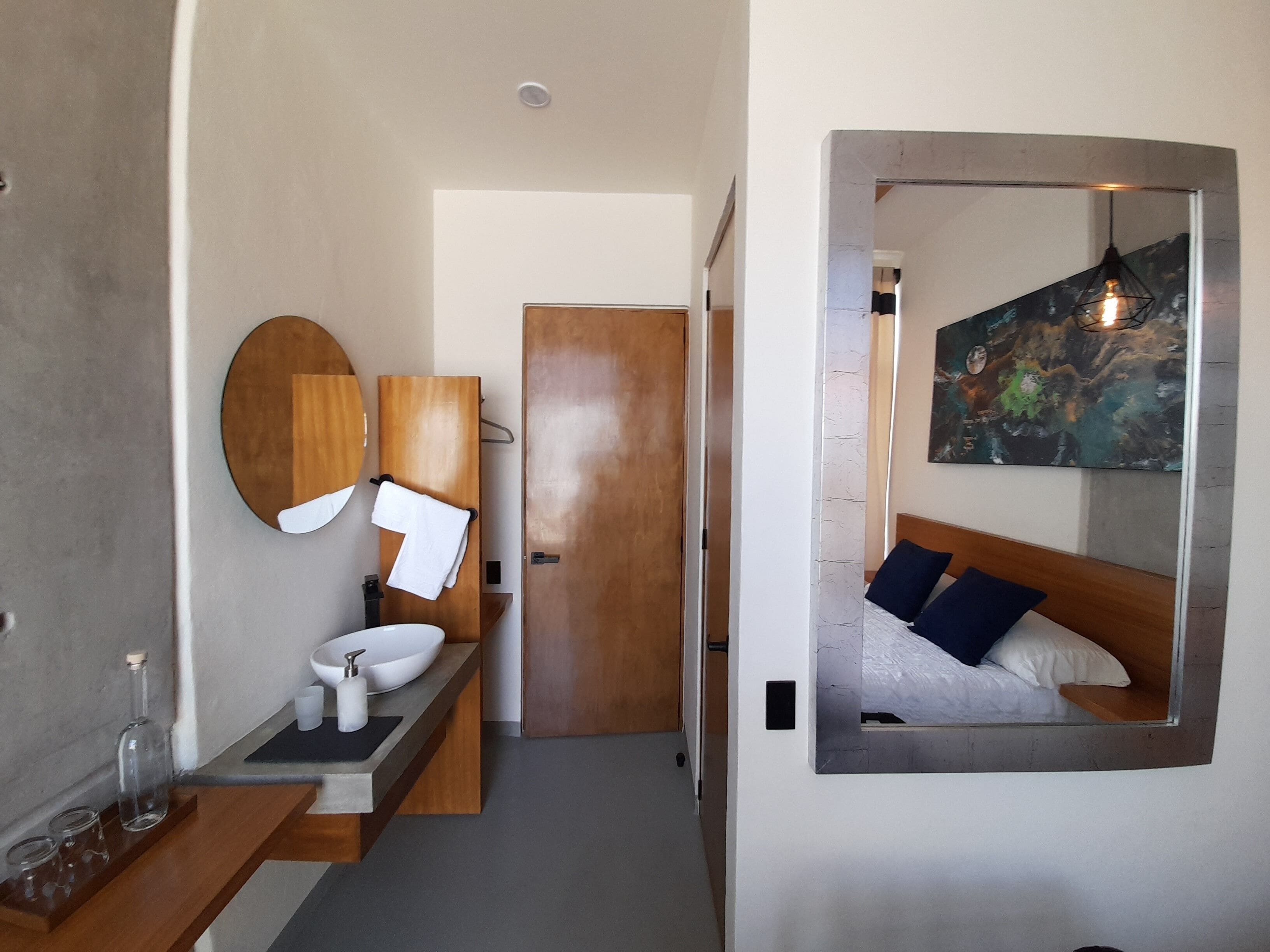 Un baño moderno con tocador de madera, un espejo redondo, inodoro y cama con espejo de cabecera.