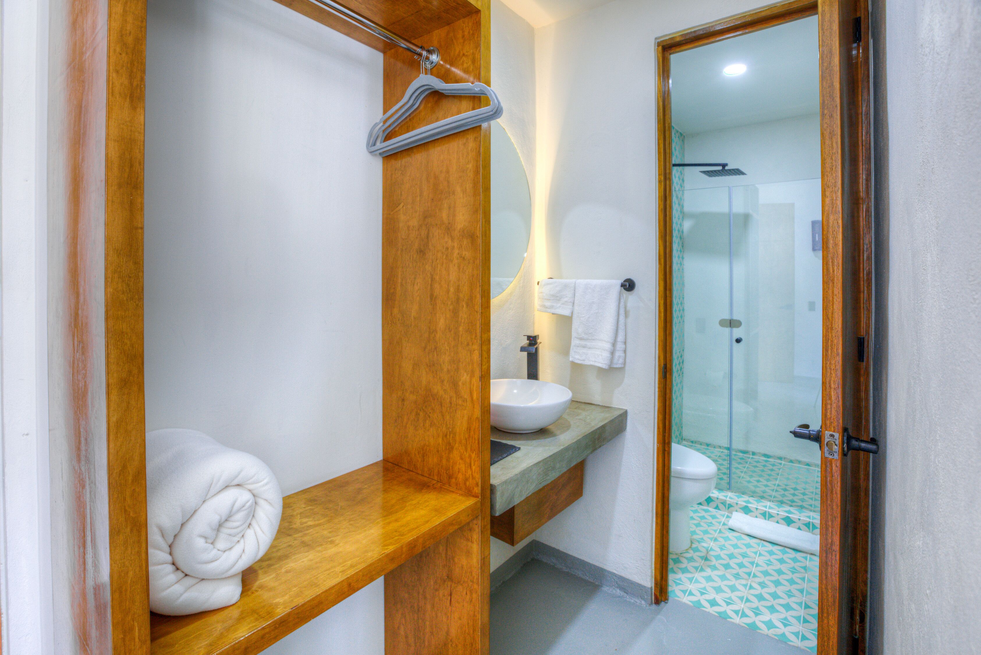 Un baño con estante de madera, lavamanos blanco y mampara de vidrio.