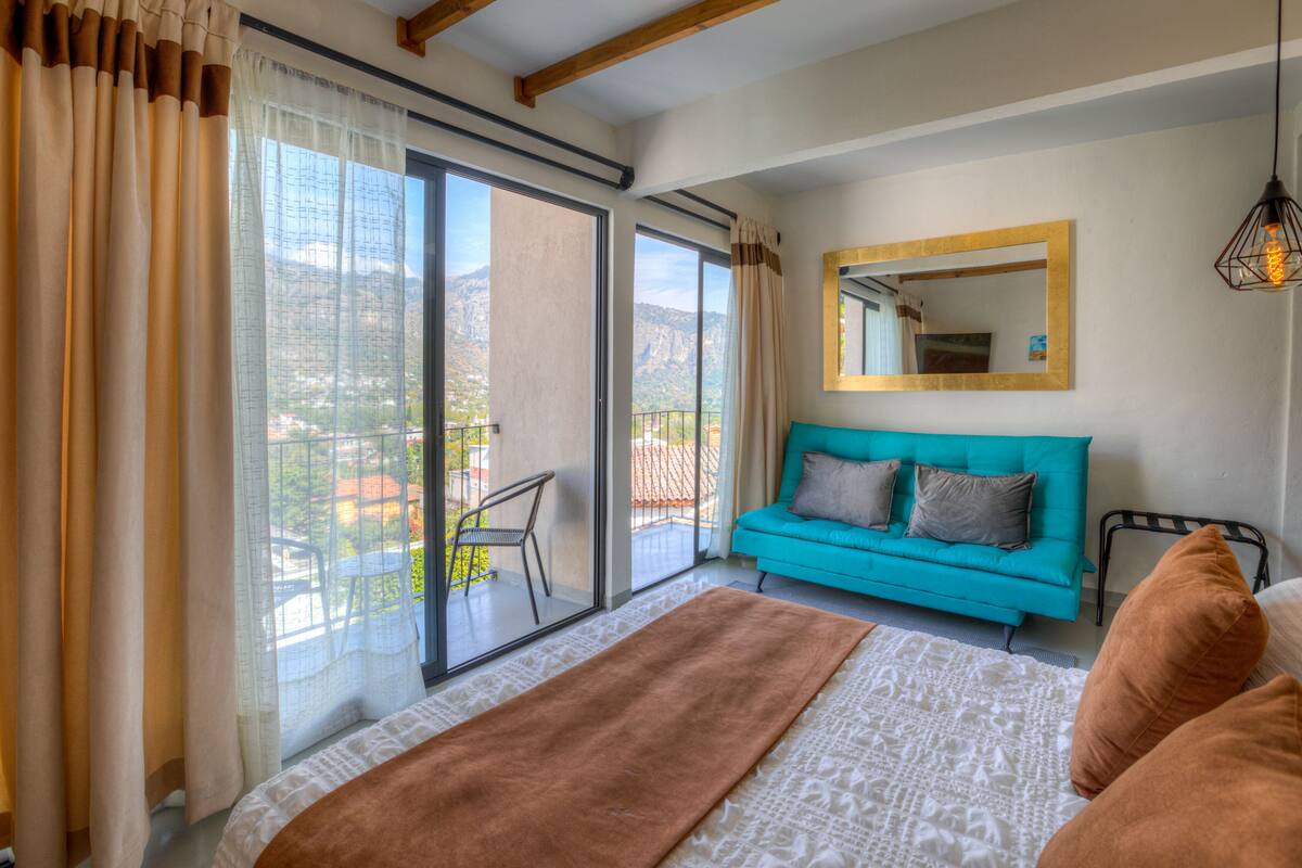 Ein Schlafzimmer mit einem großen Bett, einem Sofa, einem Spiegel und Blick ins Freie.