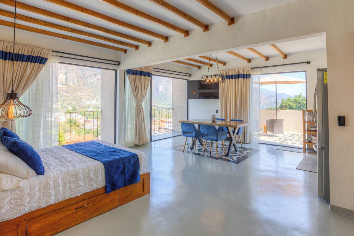 Ein geräumiges Schlafzimmer mit einem großen Bett, einem Essbereich mit blauen Stühlen und einem Balkon mit Blick auf die Berge.