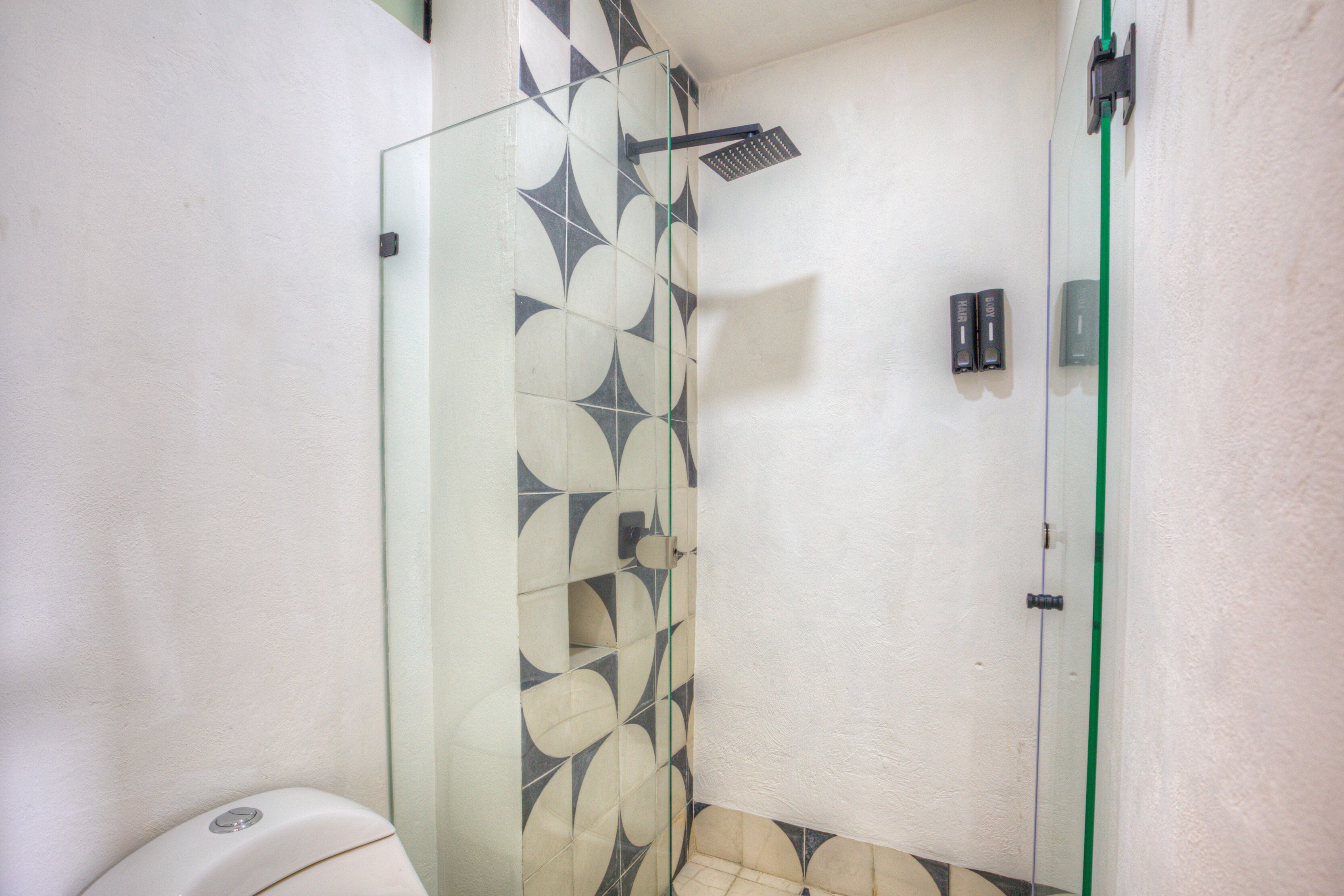 Un baño con cabina de ducha de vidrio, inodoro y pared con patrón de azulejos geométricos.