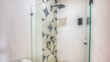 Un baño con cabina de ducha de vidrio, inodoro y pared con patrón de azulejos geométricos.
