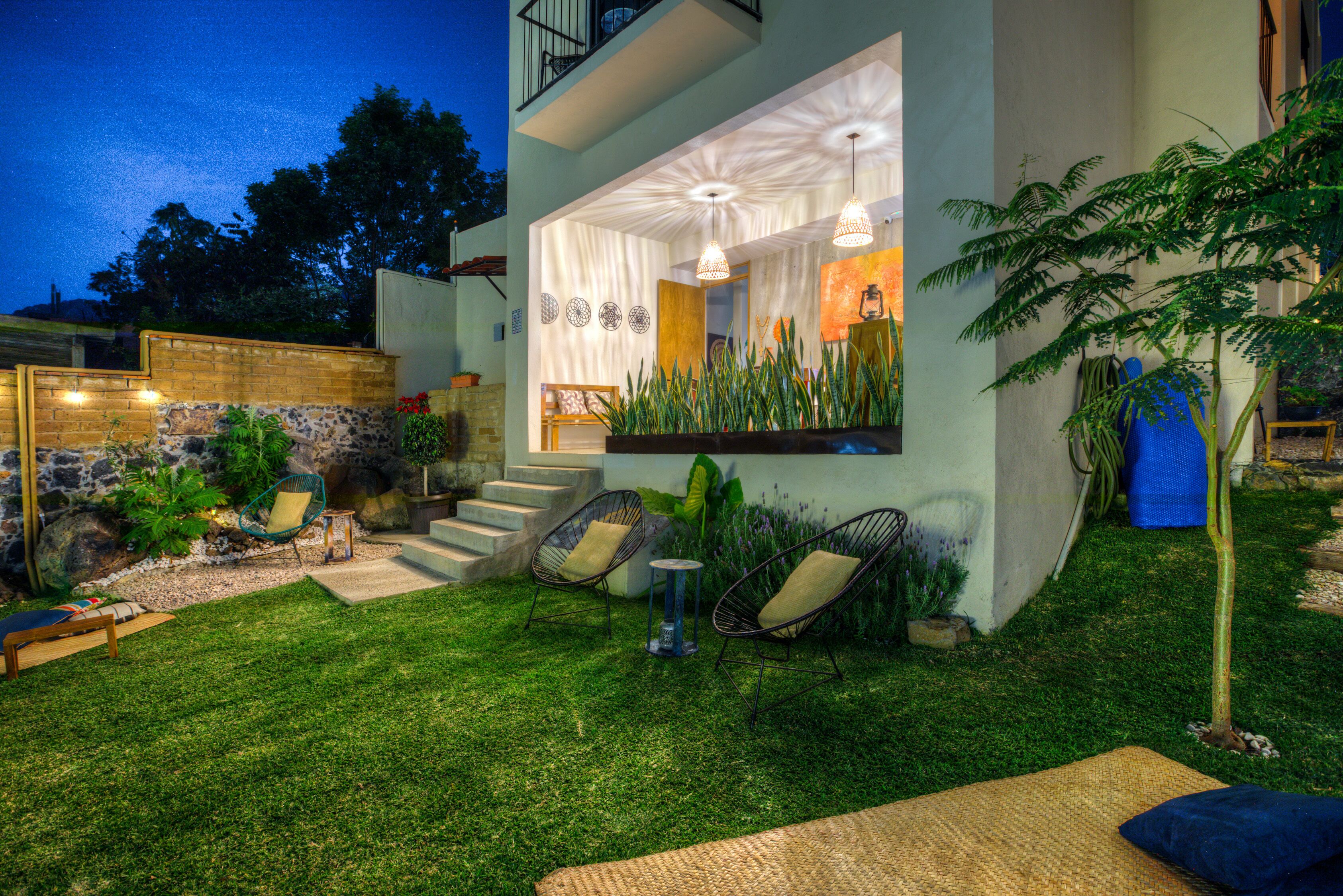 A modern house with a well-maintained lawn, outdoor seating area with chairs and a table, and a staircase leading to the entrance.