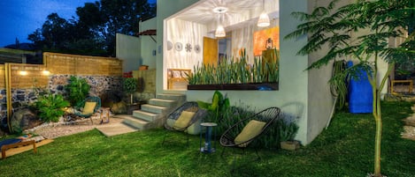 Una casa moderna con un césped cuidado, un espacio al aire libre con sillas y una mesa, y una escalera que conduce a la entrada.