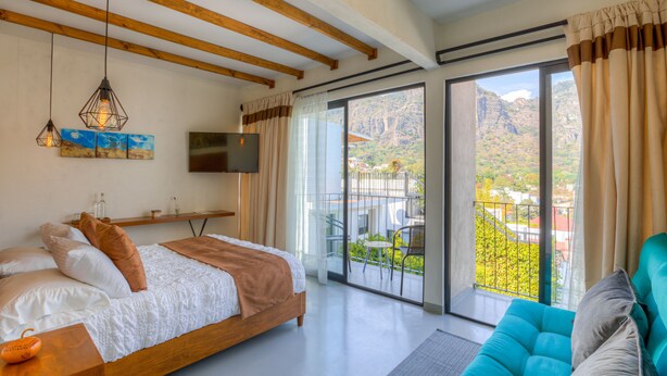 A bedroom with a bed, a TV, a sofa, and a balcony with a view of mountains.