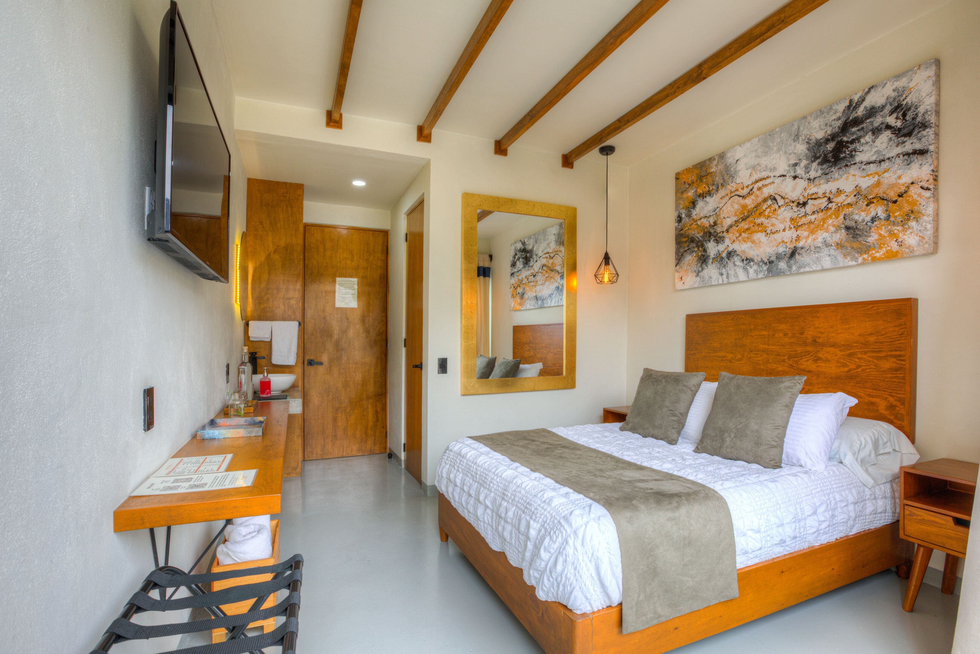Una habitación de hotel con una cama de madera, un televisor de pantalla plana montado en la pared, un cuadro abstracto grande y un escritorio de madera con una silla.