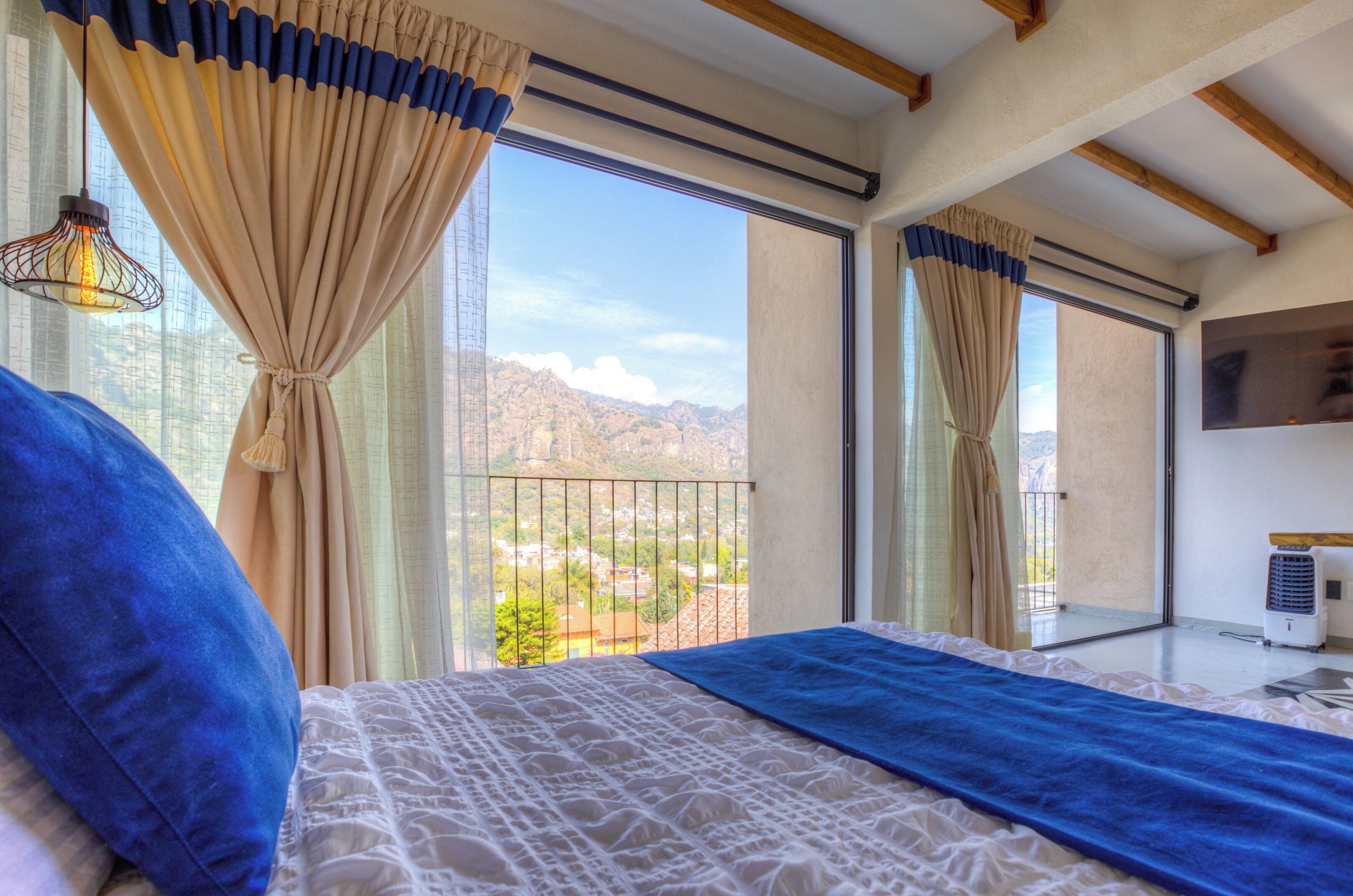 A bedroom with a bed, curtains, a window with a view of mountains, and a ceiling fan.