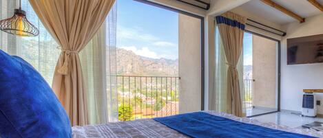 A bedroom with a bed, curtains, a window with a view of mountains, and a ceiling fan.