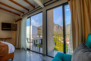 Un dormitorio con balcón, cama, televisor y vistas a la montaña.
