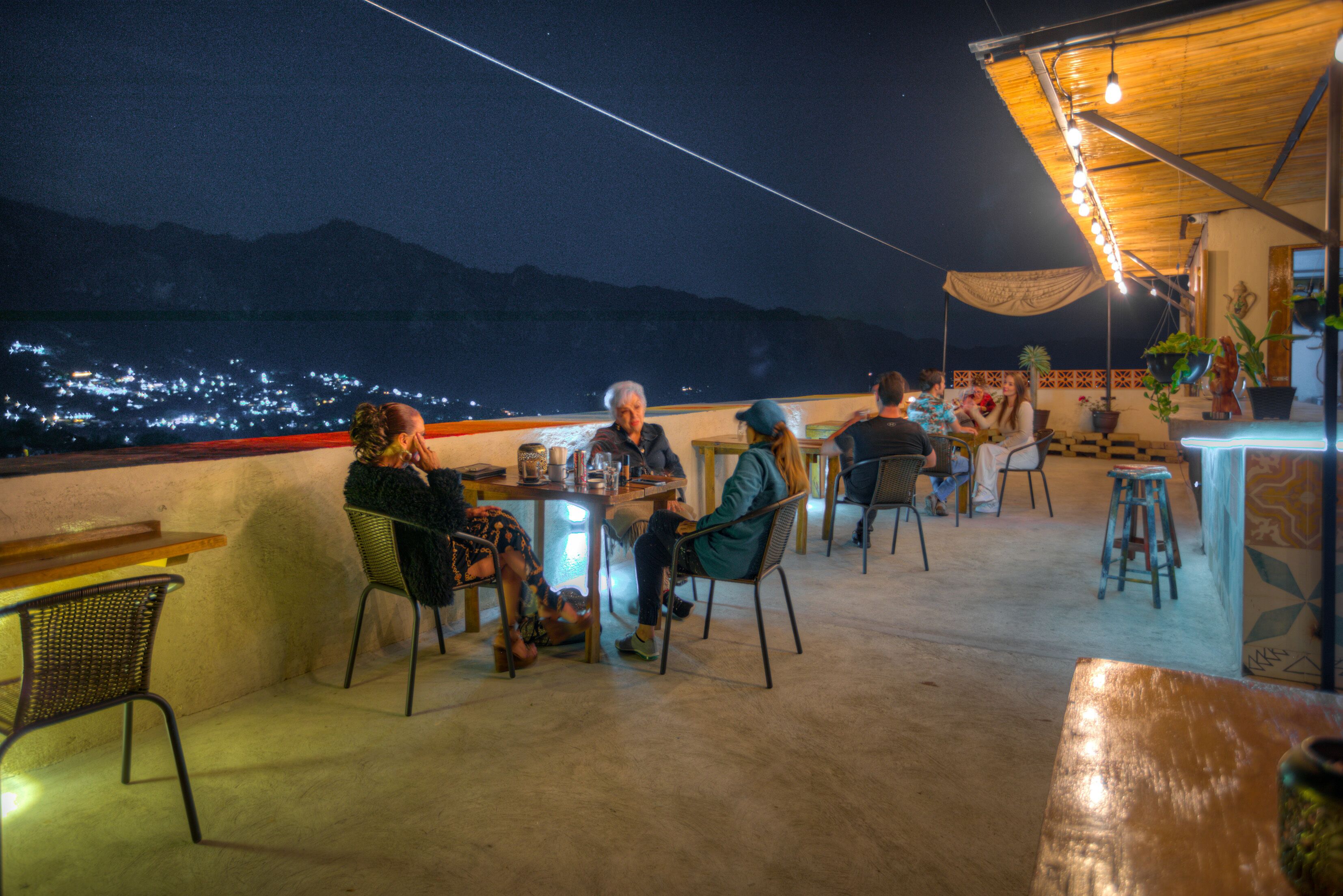 Een terras met tafels en stoelen, met uitzicht op een stadsgezicht 's nachts.