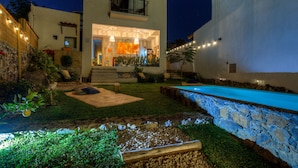 A modern two-story house with a swimming pool, outdoor seating, and a well-lit entrance.