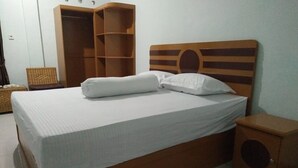 A neatly made bed with a wooden headboard, a small wooden cabinet, and a wardrobe with multiple compartments.