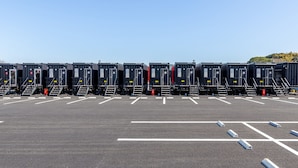 En række ensartede, transportable toiletter med numre, placeret i en parkeringsplads.