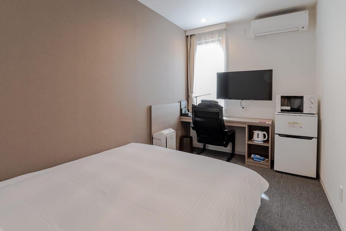 A hotel room with a bed, a desk with a chair, a television, a microwave, and a refrigerator.