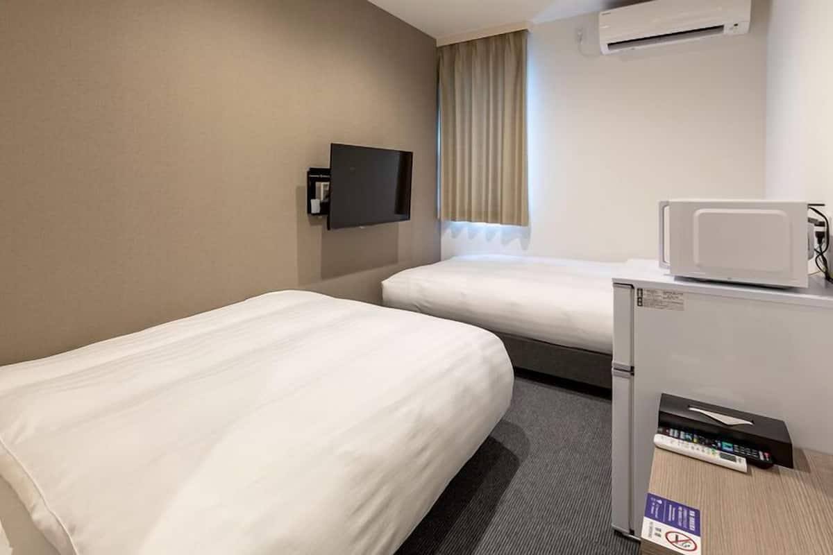 A hotel room with two single beds, a flat-screen TV mounted on the wall, a microwave, and a small refrigerator.