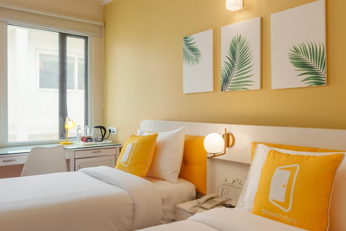 A hotel room with two beds, a desk with a lamp, a phone, and wall art.