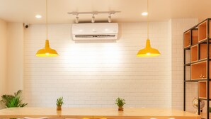 Una cocina moderna con pared de ladrillo blanco, una mesa de madera y cuatro sillas. Hay dos lámparas colgantes, un equipo de aire acondicionado y una estantería con un globo terráqueo.