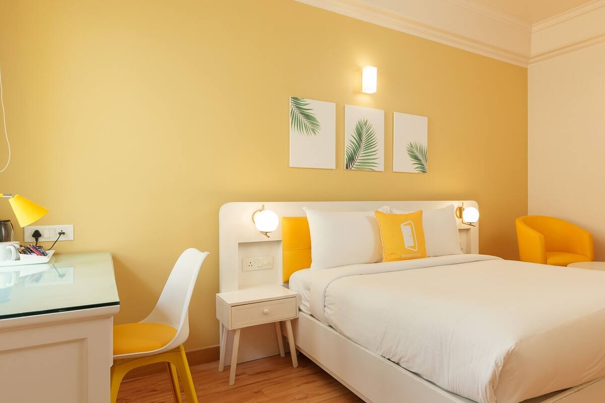 A hotel room with a bed, a desk, a chair, and a nightstand. There are three wall-mounted light fixtures and a wall-mounted artwork.