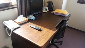 Un escritorio de madera con un teléfono, un control remoto, una caja de pañuelos, una cafetera y una pila de toallas dobladas.