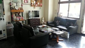 Una sala de estar con un sofá, un sillón, un reposapiés y una mesa de centro. Se observa un televisor, un mueble y una ventana con vistas al exterior.