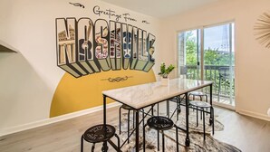 A dining area with a large table and chairs, a mural with the word "HARBOR," and a view of greenery through a large window.