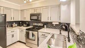 A modern kitchen with white cabinets, a black stove, a microwave, and a sink.