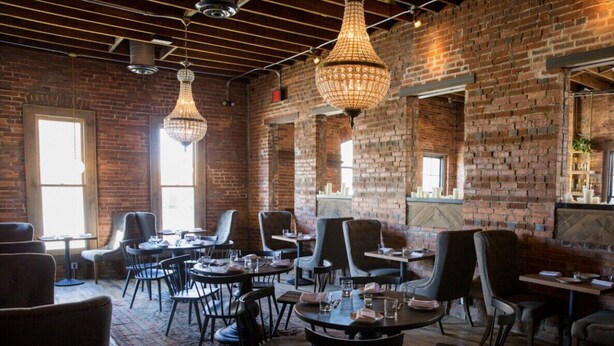 A restaurant with brick walls, hanging crystal chandeliers, and round tables with chairs.